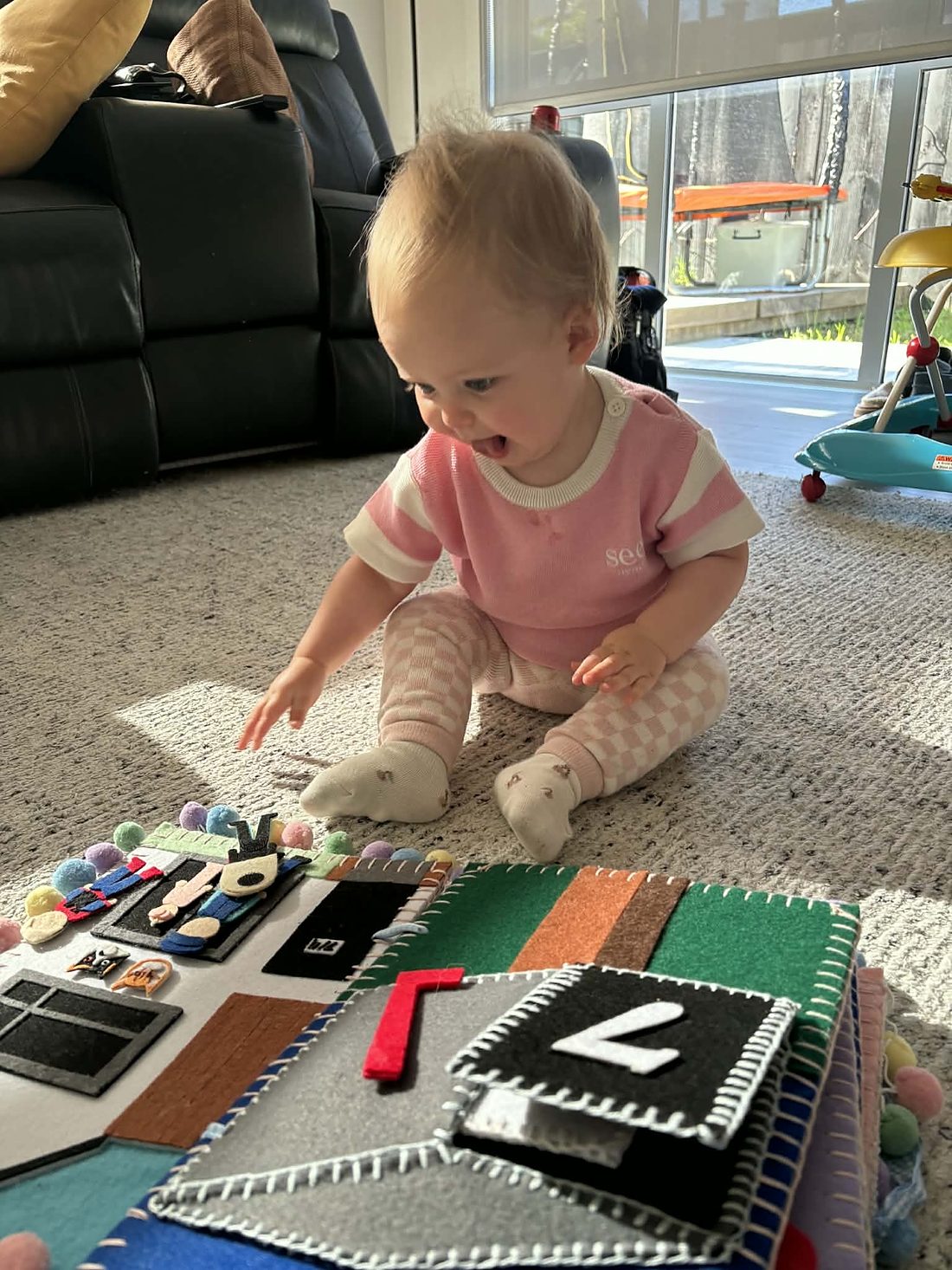 A one-year-old girl delightedly playing with her hand-crafted felt busy book on the living room floor