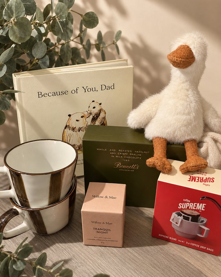 A gift for a new father: a keepsake book, a soft duckling toy, stacked mugs, chocolate, coffee and a candle