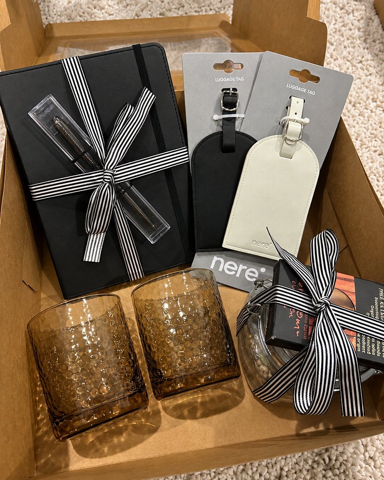 A gift of a black notebook and pen tied with striped ribbon, two leather luggage tags and amber tumblers