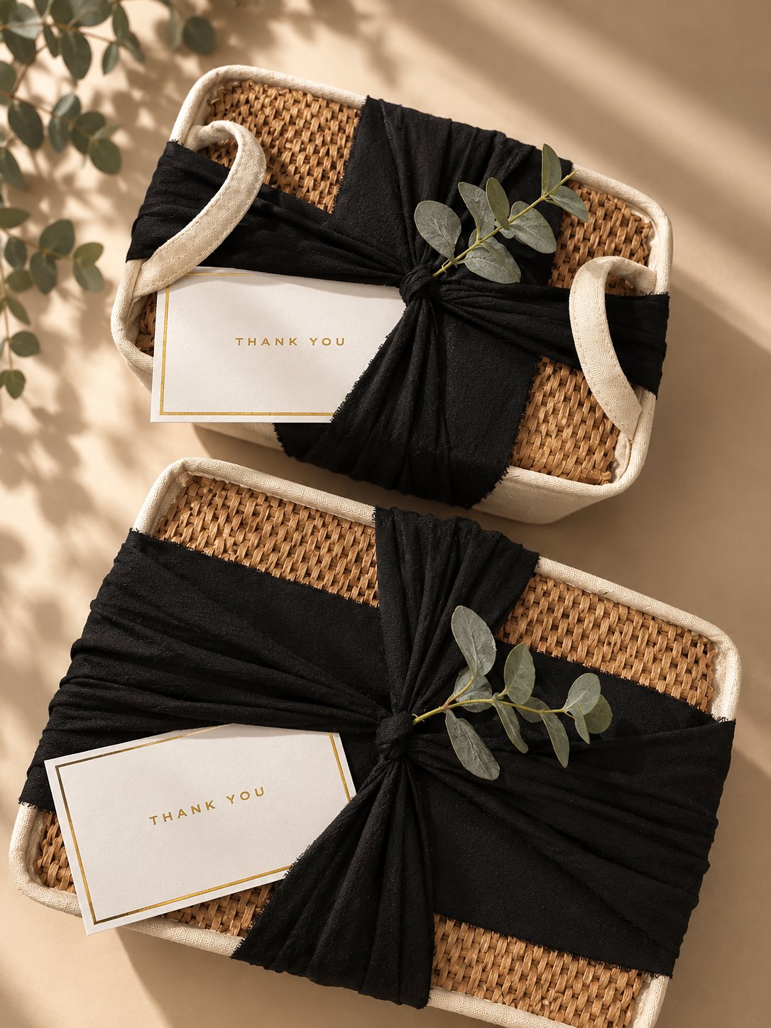 Two woven gift baskets wrapped in black fabric, each tied with eucalyptus and finished with a thank you card